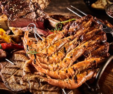 Large platter of barbecue beef, shrimps and skewered vegetables served on table with oil, hot peppers and seasonings